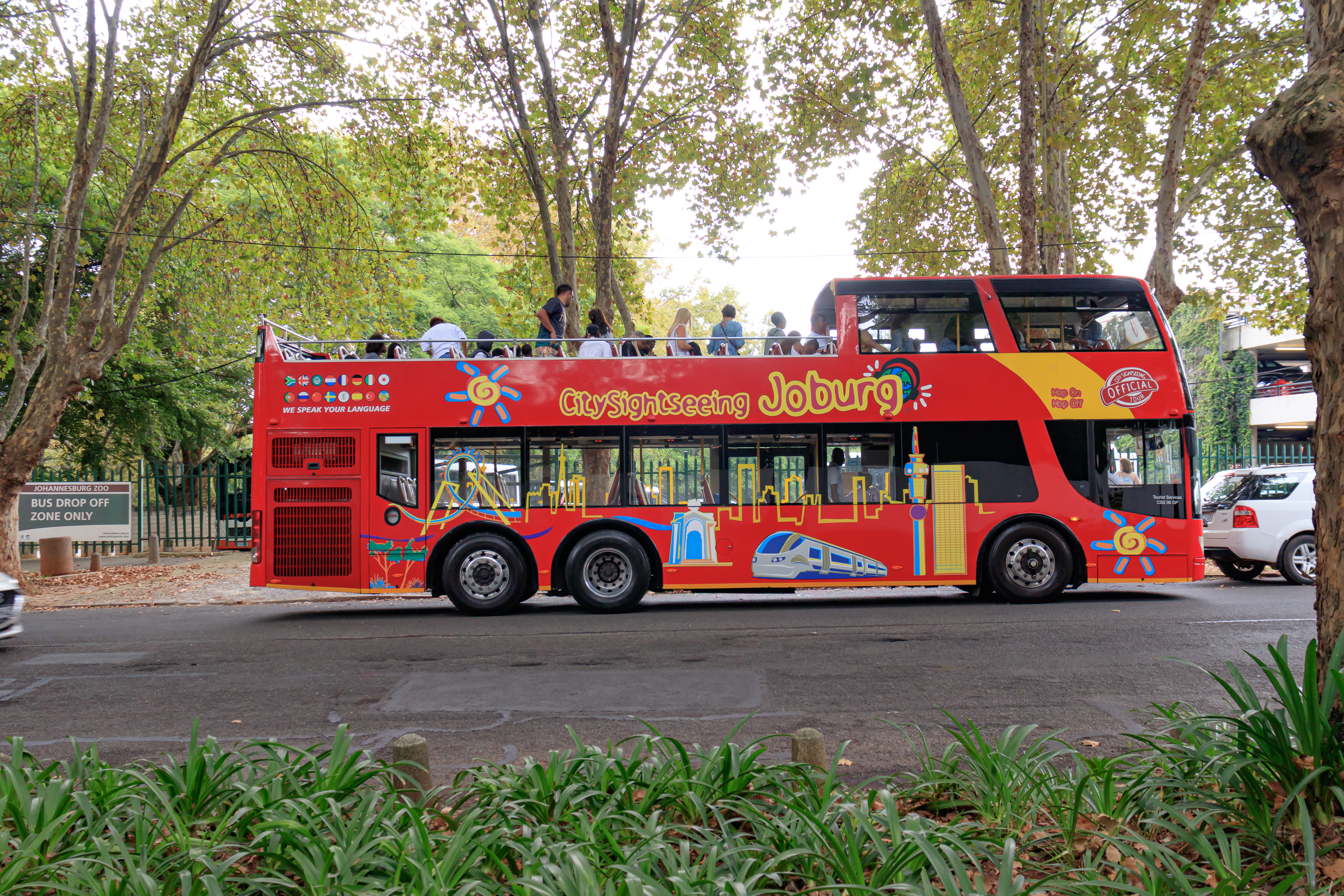 Full side view of a red City Sightseeing Johannesburg bus with passengers on the open top deck